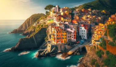 Vibrant, colorful houses of Cinque Terre perched on cliffs overlooking the blue Mediterranean Sea, with lush greenery and a clear sky creating a picturesque coastal scene.